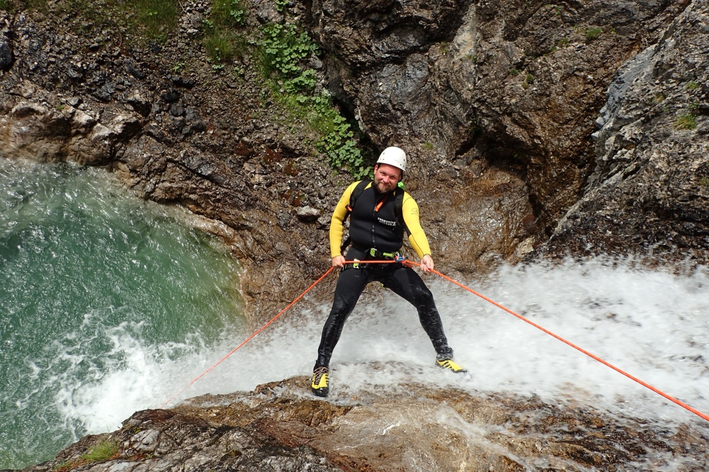 Un pratiquant équipé baudrier, casque et corde en pleine descente en rappel